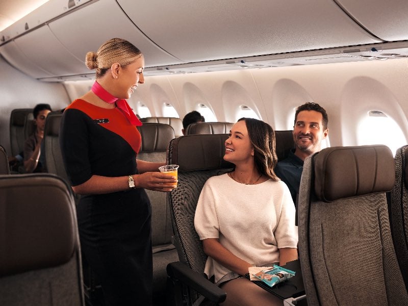 Qantas cabin crew giving orange juice to a couple on an Airbus A220 in economy