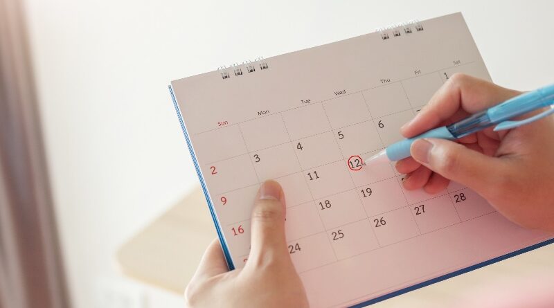 Hand with pen mark at 12th on calendar date with red circle