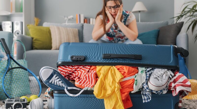 Stressed woman sitting on the couch at home and big overfilled trolley bag, she is packing for a vacation