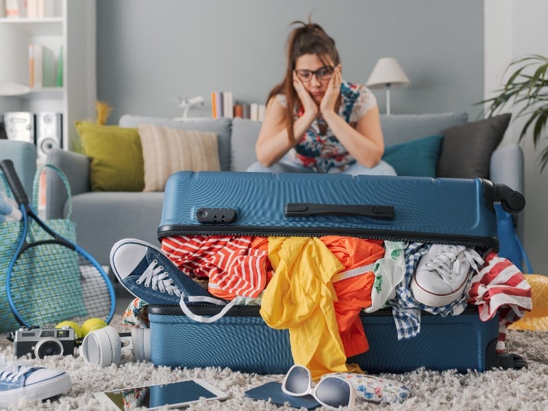 Stressed woman sitting on the couch at home and big overfilled trolley bag, she is packing for a vacation